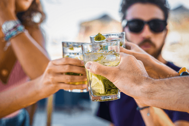 closeup on the hand of young people clinking glasses of cocktails celebrating friendship together on the beach cafe.