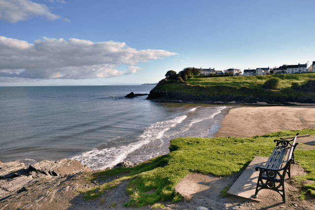 view of the Blue Flag beach at Aberporth, Ceredigion, Wales, with waves breaking onto the sandy shore, and a headland jutting into the sea.