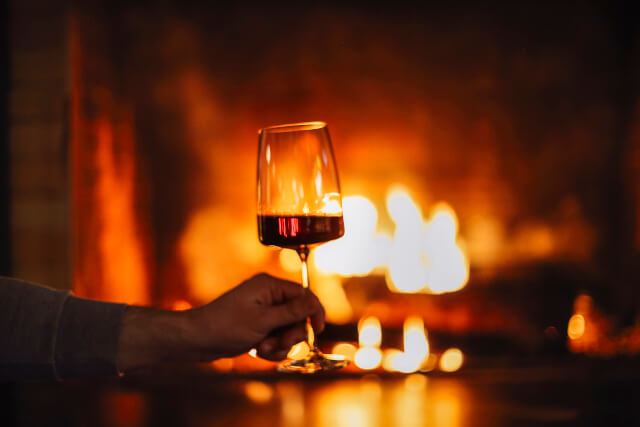 Man enjoying a glass of red wine by the fire.