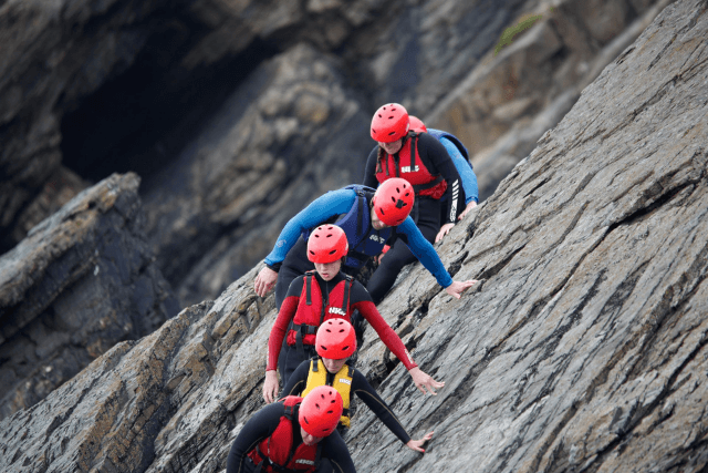 A group of children climbing across cliffs whilst coasteering