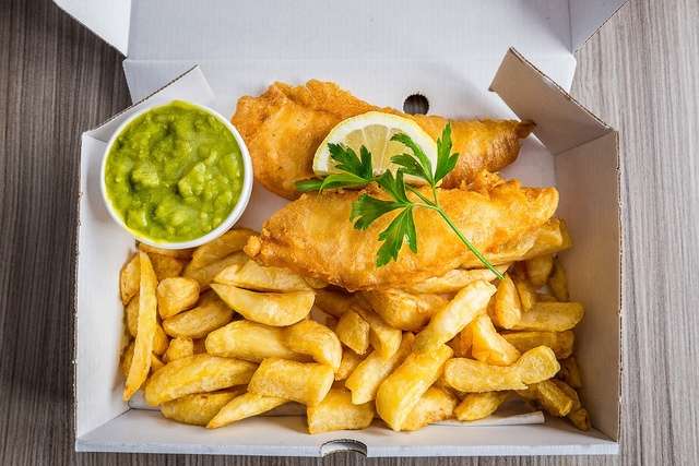 A portion of fish and chips with a slice of lemon and mushy peas.